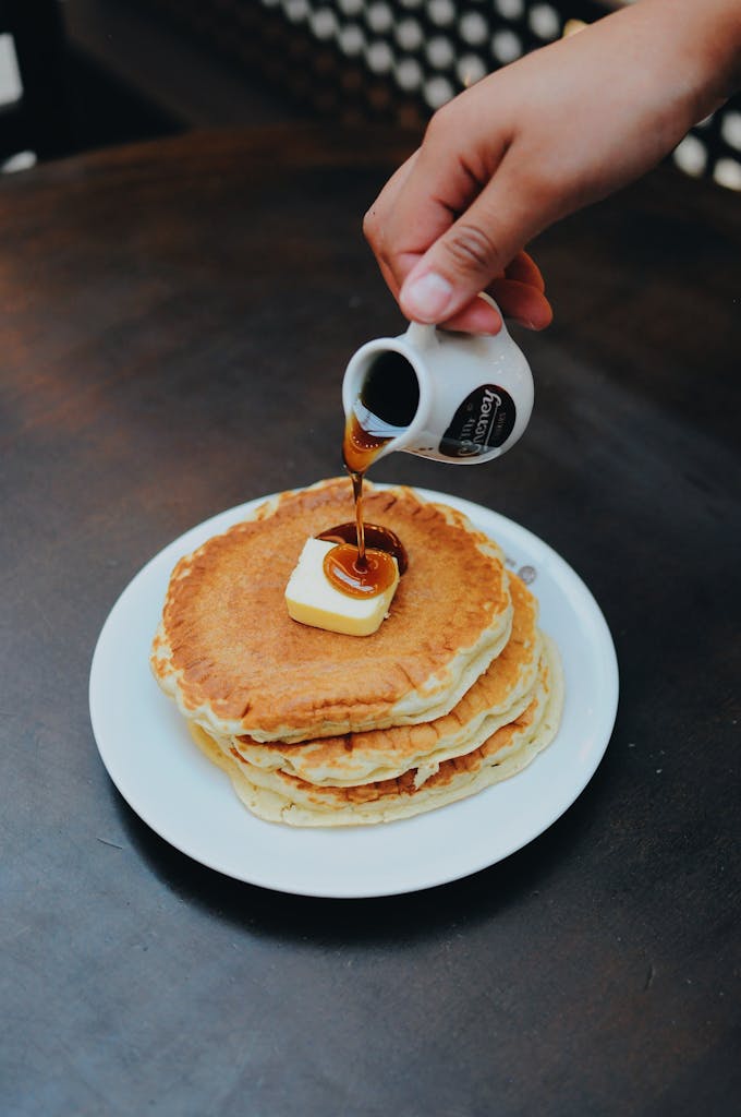 Person Pouring Syrup on Pancake